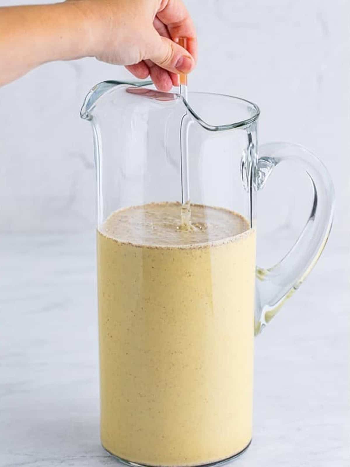 A glass pitcher filled with creamy eggnog Christmas punch ready to chill.