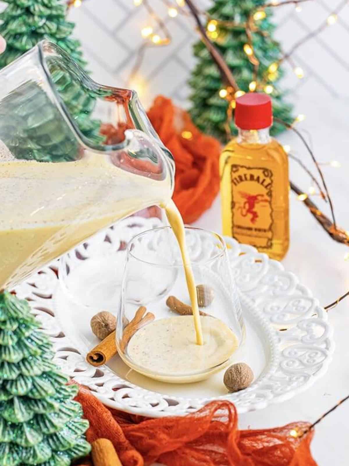 Pouring Christmas punch from the pitcher into a serving glass surrounded by holiday decor.