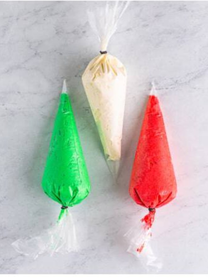Red, green, and white frosting in piping bags for filling the christmas sandwich cookies.