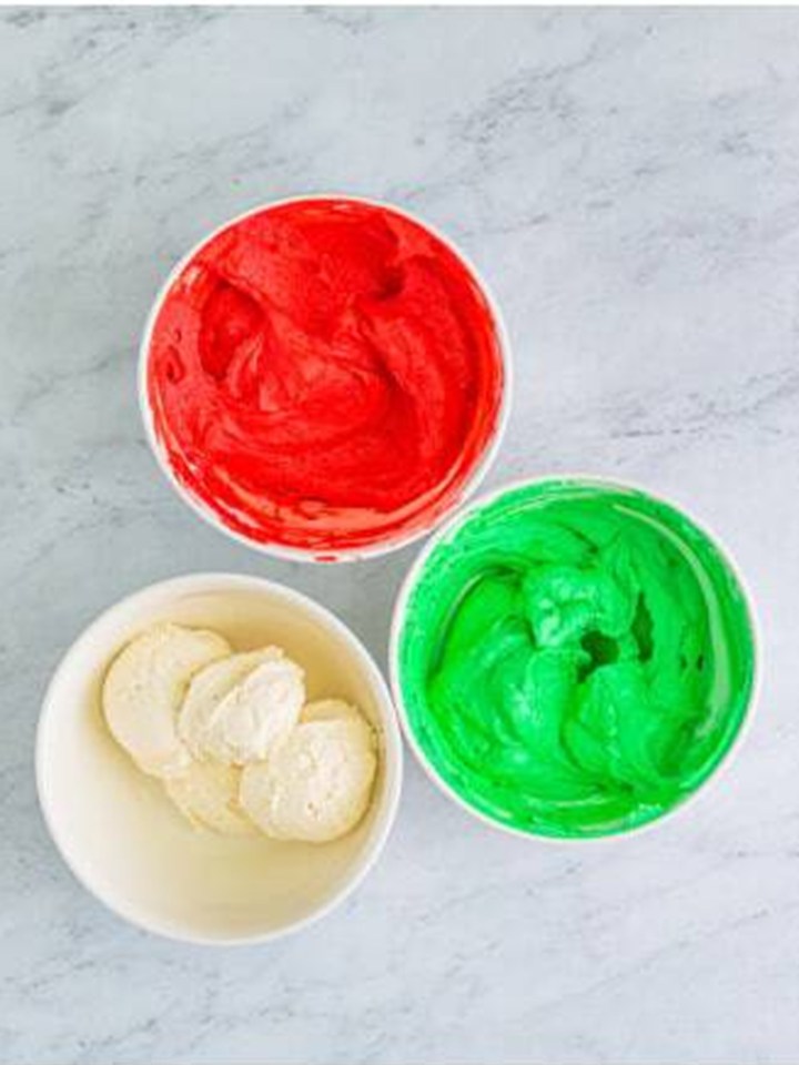 Buttercream filling divided into three bowls, one tinted red and one tinted green.