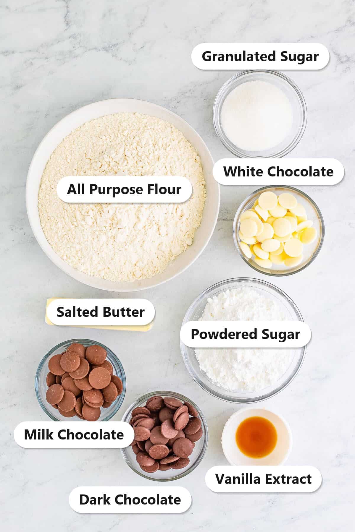 Labeled ingredients for Christmas shortbread cookies: flour, salted butter, powdered sugar, granulated sugar, vanilla, and white, milk, and dark chocolate.
