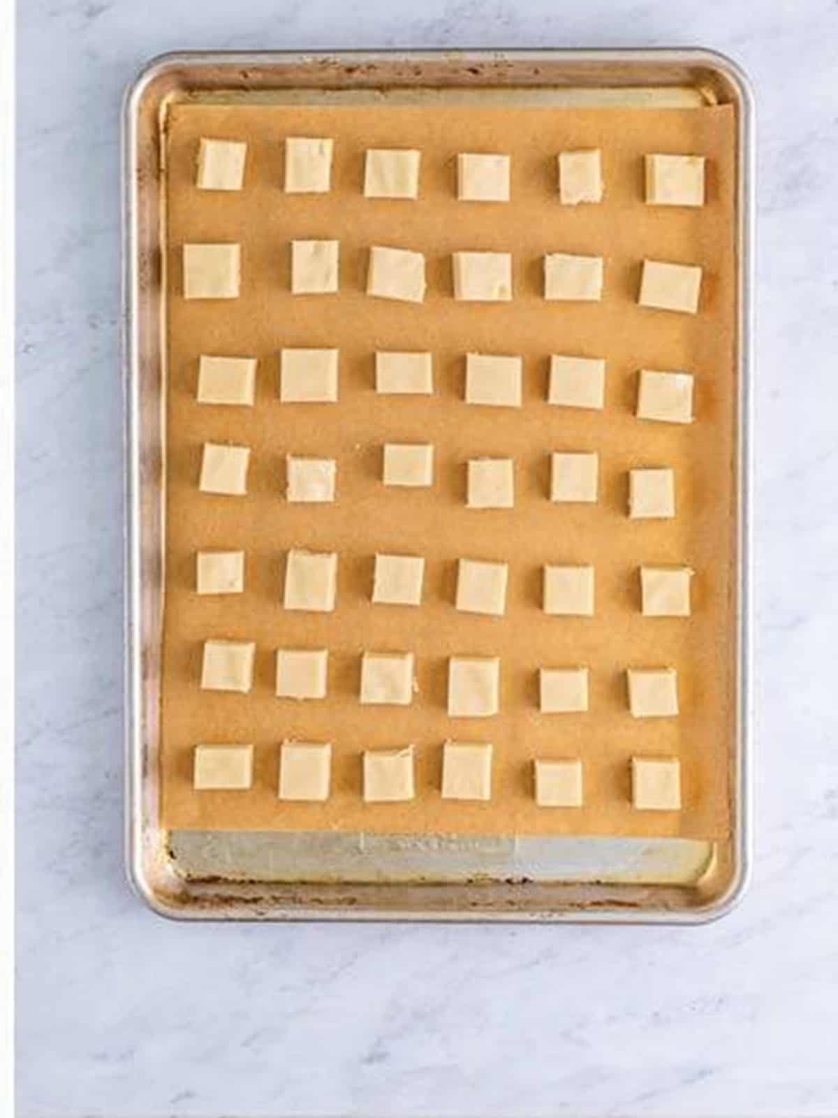 Chilled shortbread dough cut into half inch squares arranged on a parchment lined sheet tray.