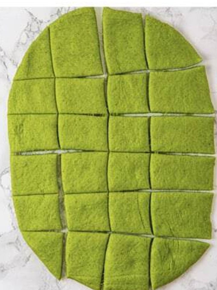 Rolled out green spinach dough cut into 20 equal portions.
