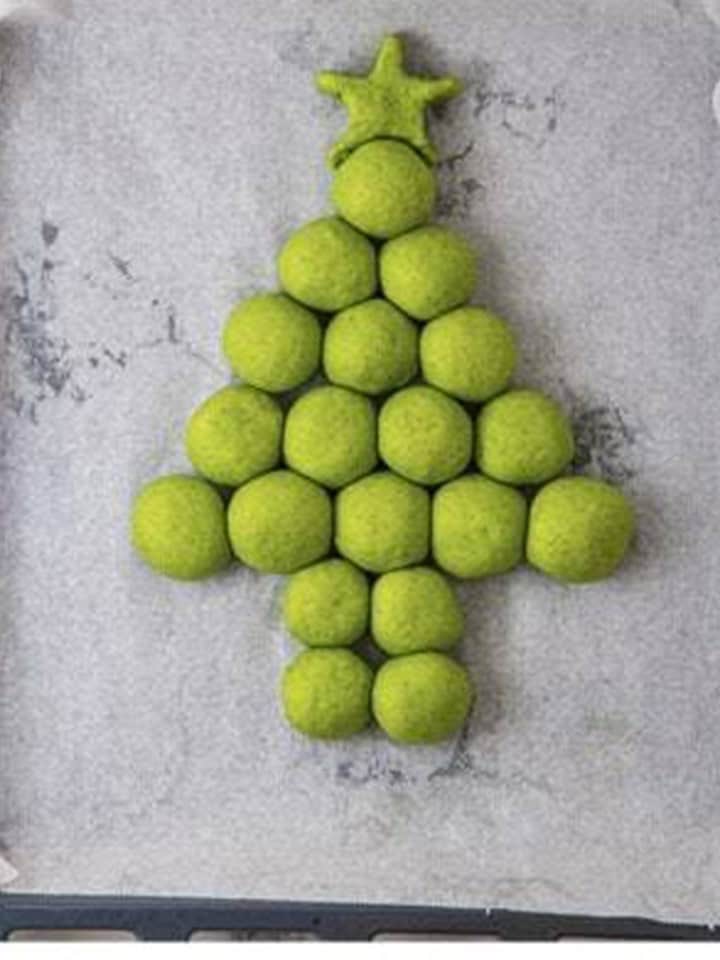 Green dough balls arranged in a Christmas tree shape with a star on a parchment lined tray.