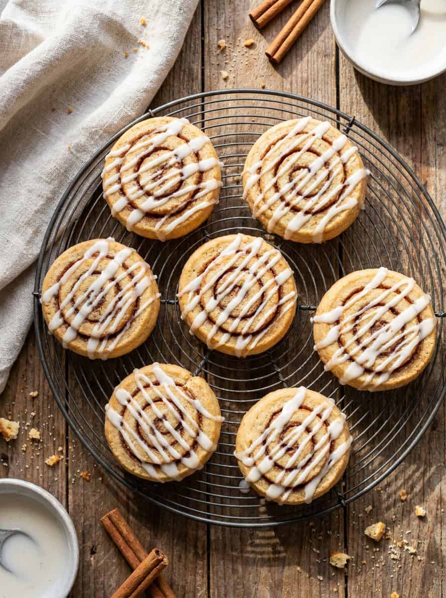 Baked cinnamon roll cookies drizzled with white vanilla glaze cooling on a wire rack.