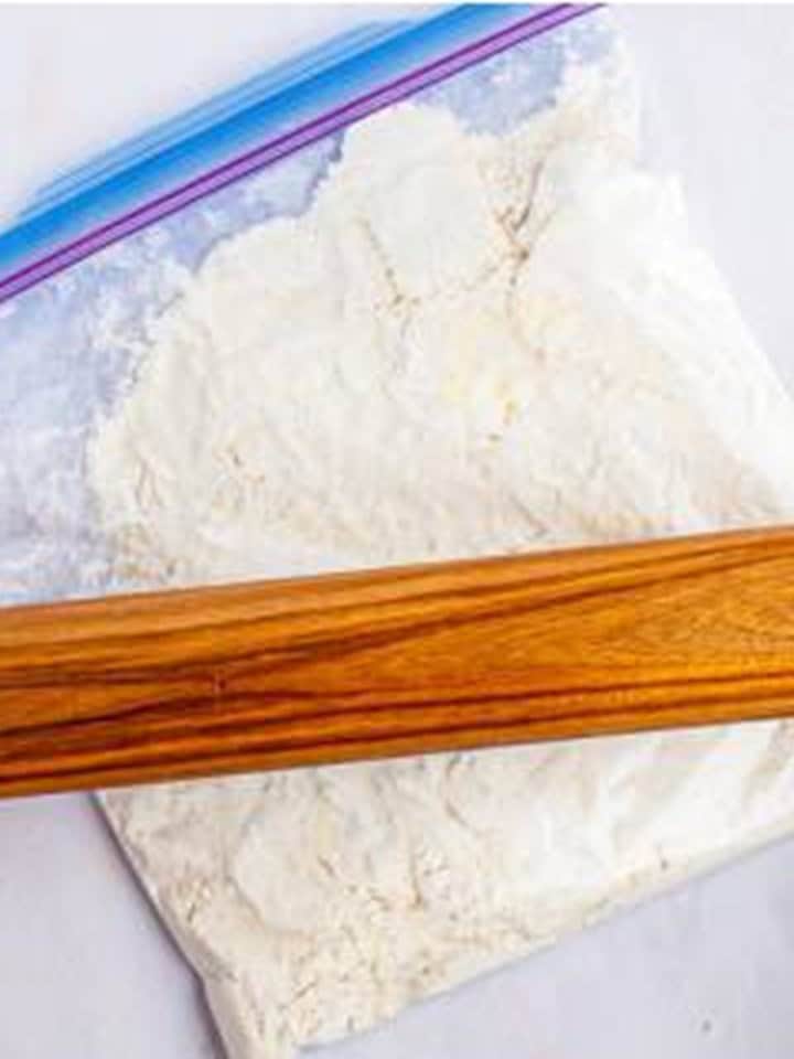 Rolling pin flattening butter into the flour mixture inside a plastic bag for Cinnamon Rolls dough.
