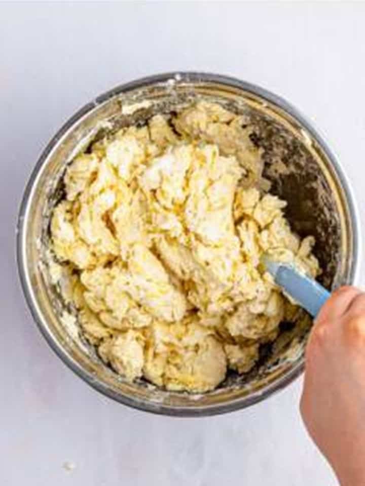Crumbly Cinnamon Rolls dough being mixed with a spatula in a metal bowl.