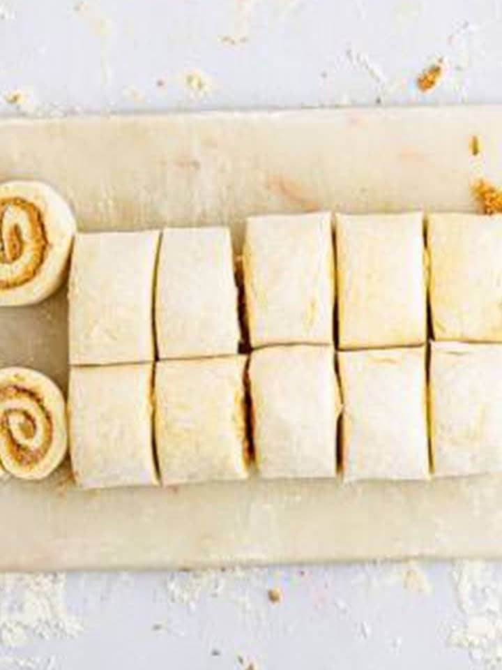 Cinnamon Rolls dough log cut into twelve even pieces on a floured board.