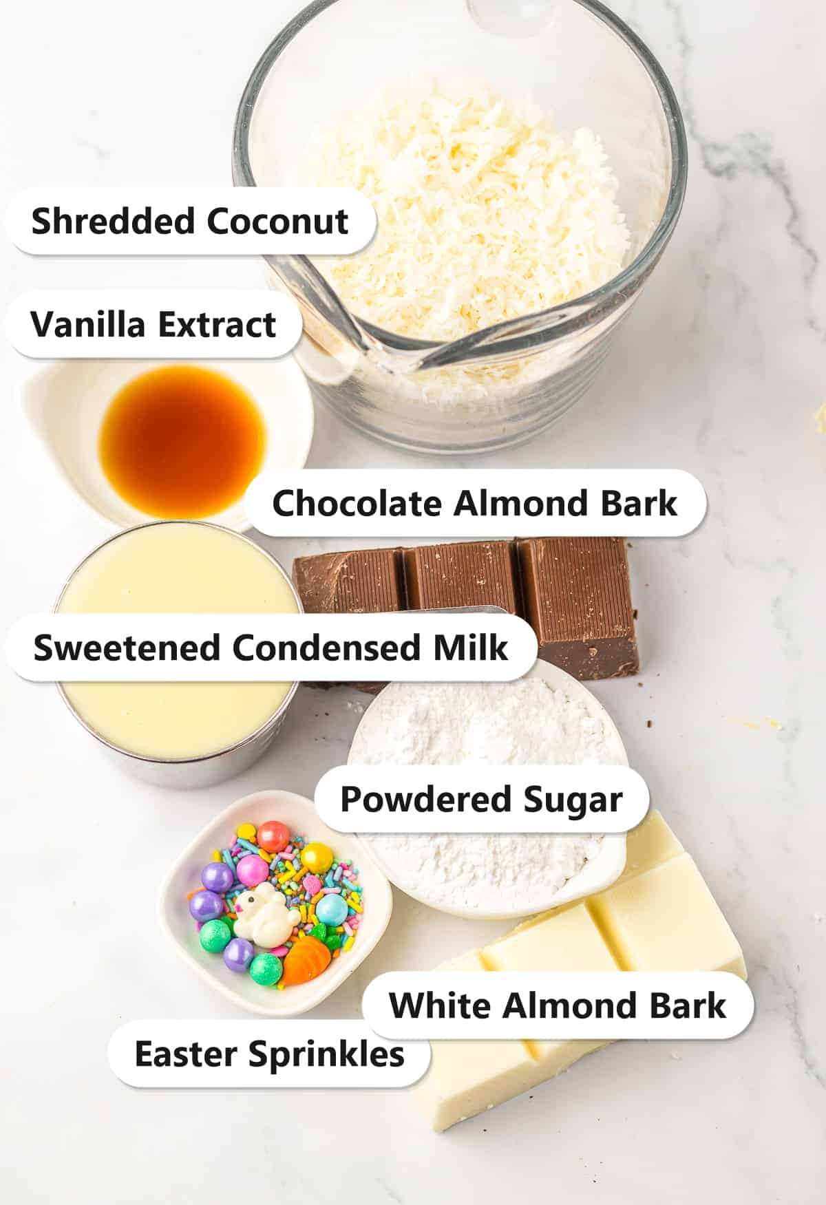 Labeled ingredients for Coconut Candy including shredded coconut, sweetened condensed milk, powdered sugar, vanilla extract, chocolate and white almond bark, and Easter sprinkles.