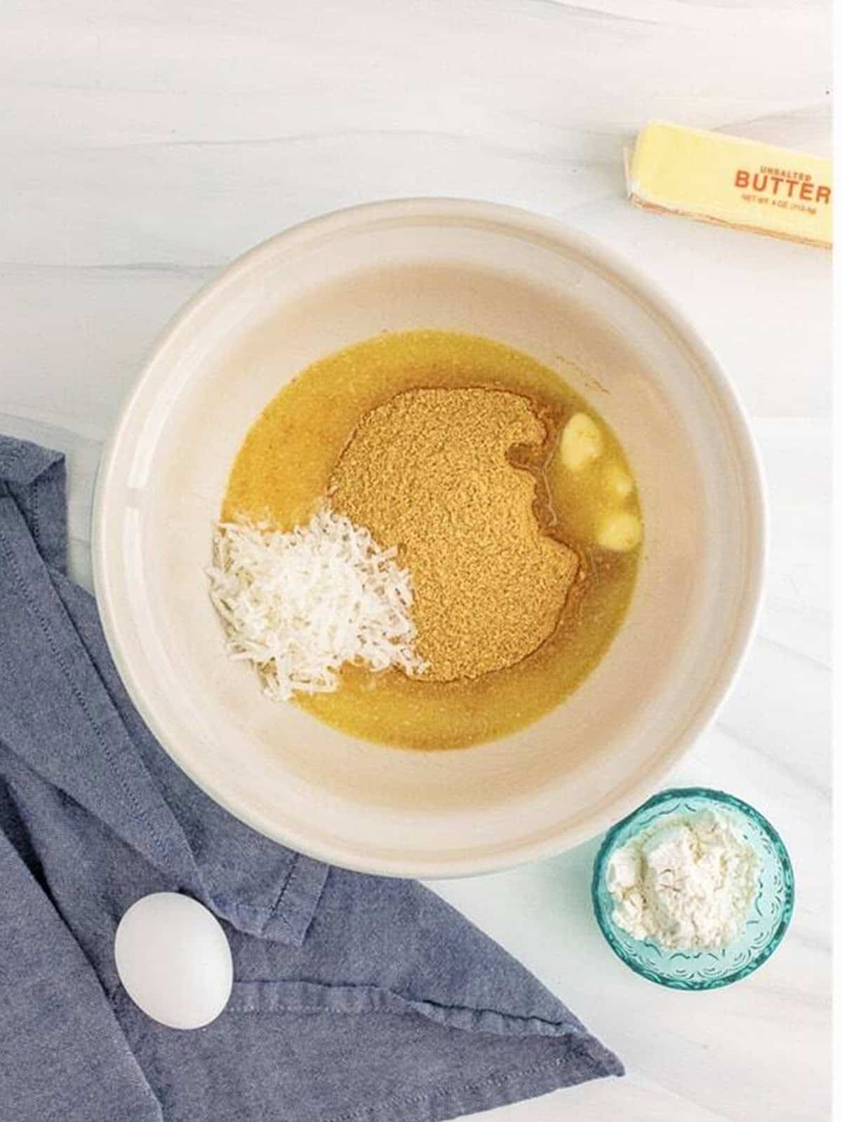 Graham cracker crumbs, coconut flakes, and melted butter in a mixing bowl for the coconut cheesecake crust.