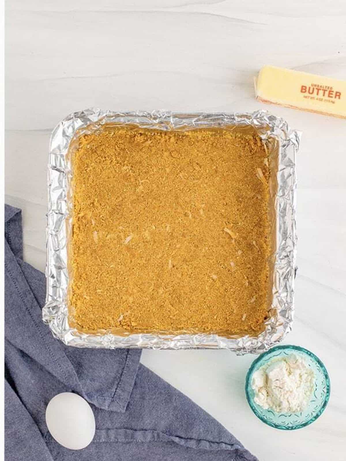 The coconut graham cracker crust pressed evenly into a foil lined square baking pan.