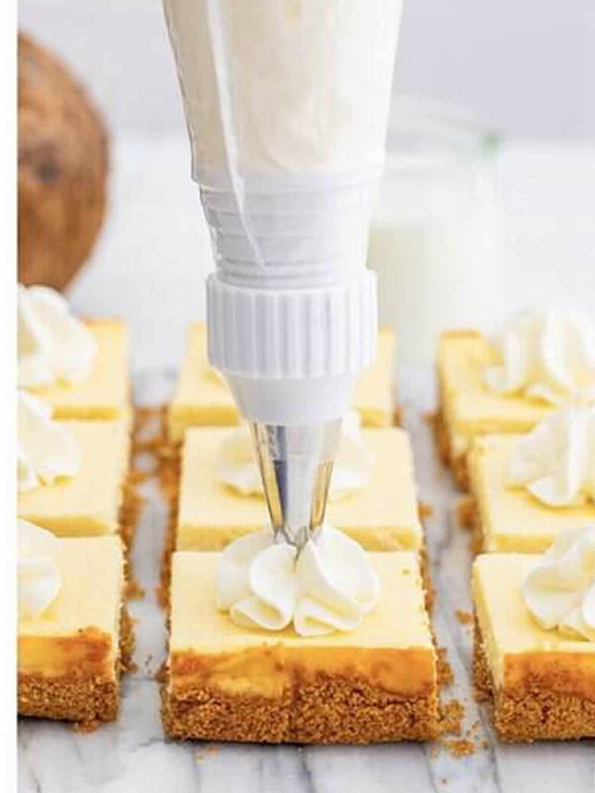 Piping whipped cream swirls onto the chilled and cut coconut cheesecake bars.