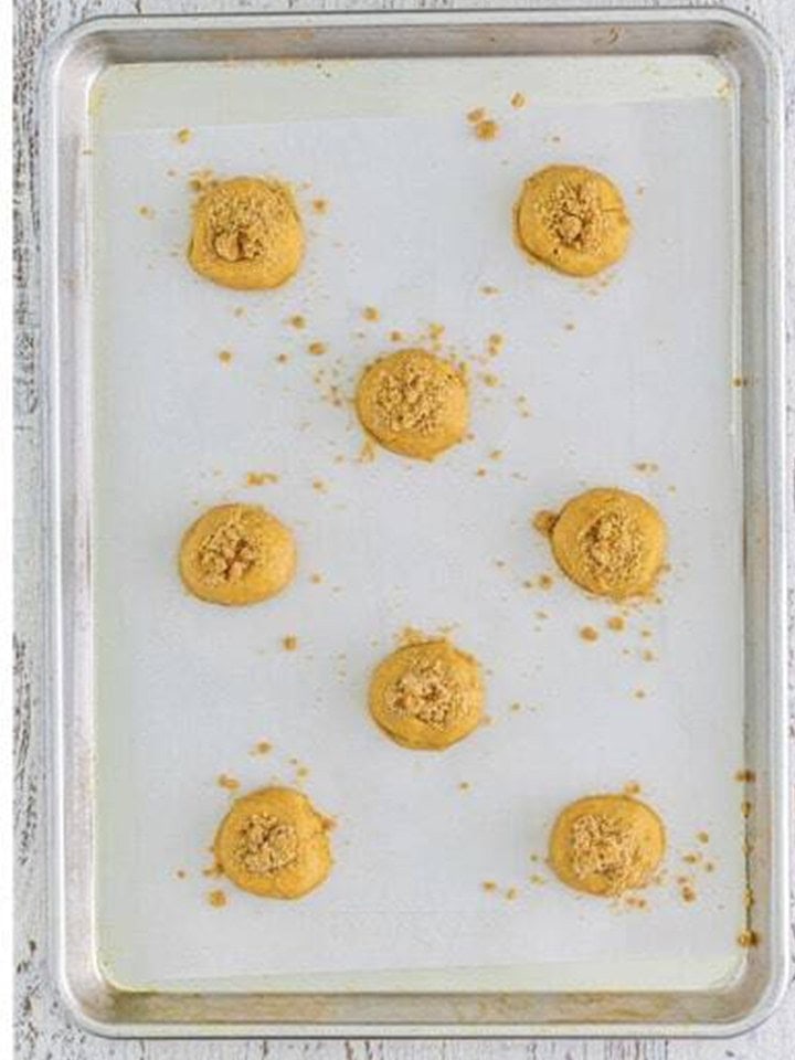 Indented coffee cake cookies filled with cinnamon crumble on a baking sheet.
