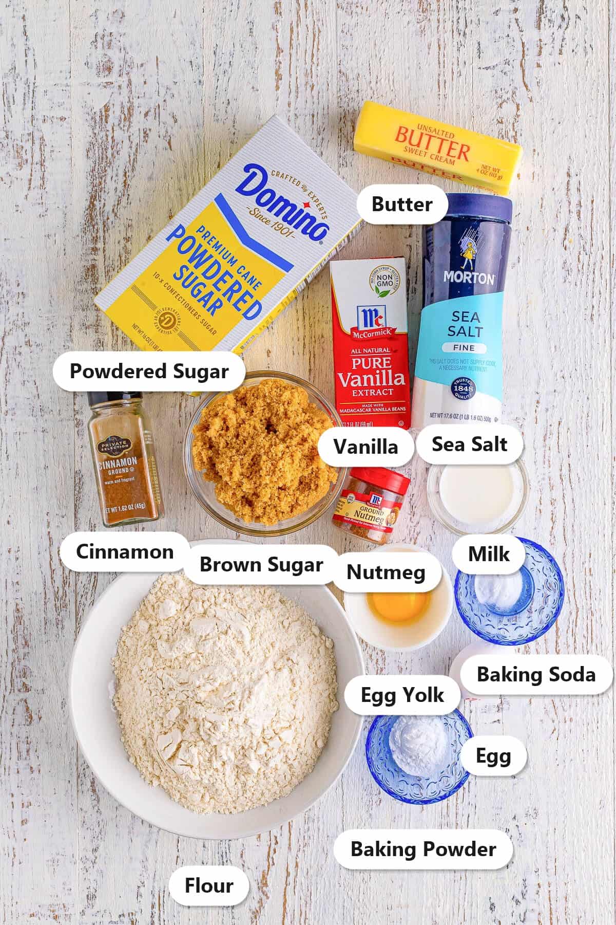 Ingredients to make coffee cake cookies: flour, butter, brown sugar, egg, egg yolk, vanilla, cinnamon, nutmeg, sea salt, baking powder, baking soda, powdered sugar, and milk.