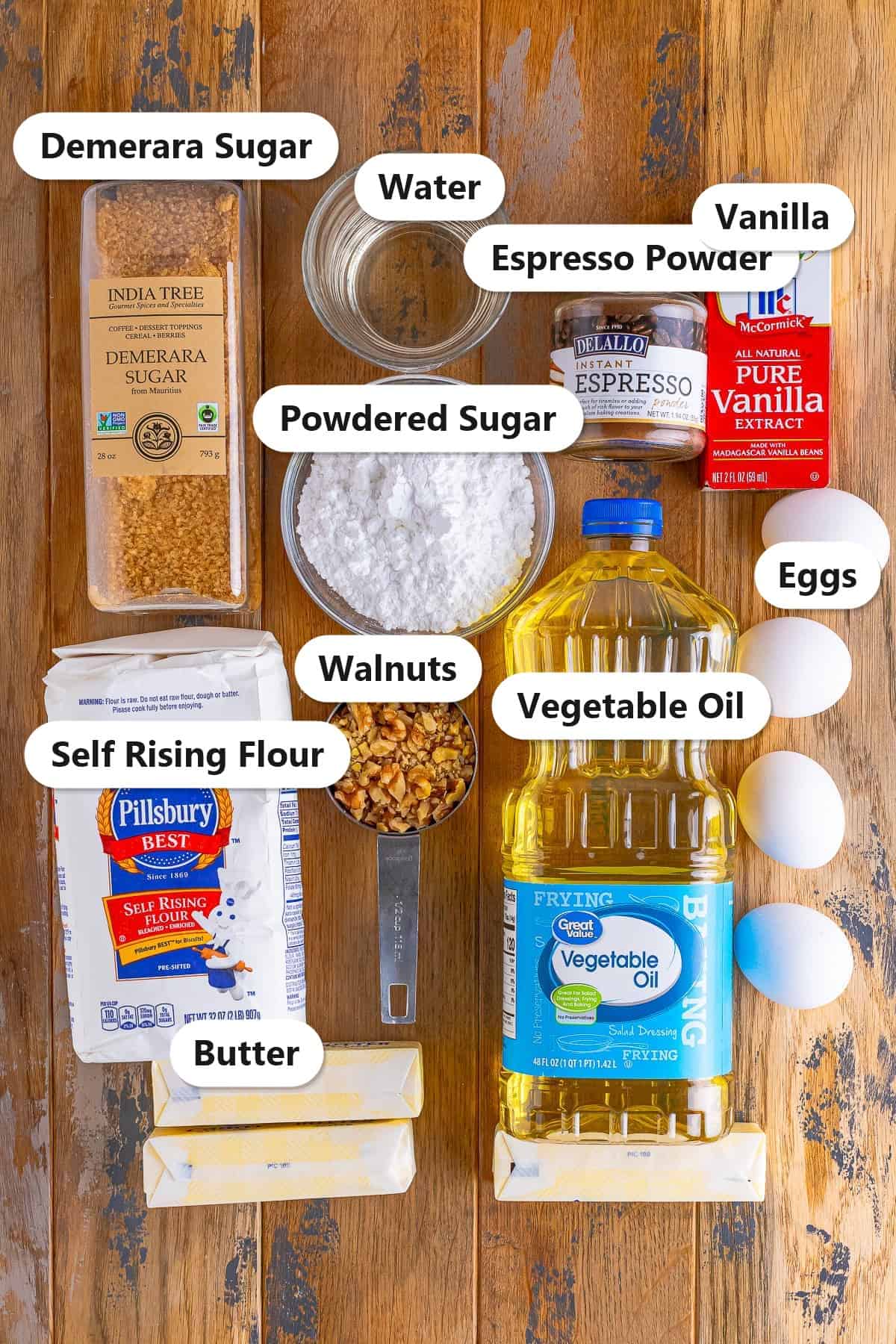 Labeled ingredients for coffee walnut cake including self rising flour, demerara sugar, butter, vegetable oil, eggs, espresso powder, walnuts, powdered sugar, vanilla, and water.
