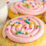 A confetti cake cookie topped with a swirl of pink cream cheese frosting and pastel sprinkles.