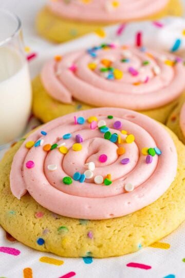 A confetti cake cookie topped with a swirl of pink cream cheese frosting and pastel sprinkles.