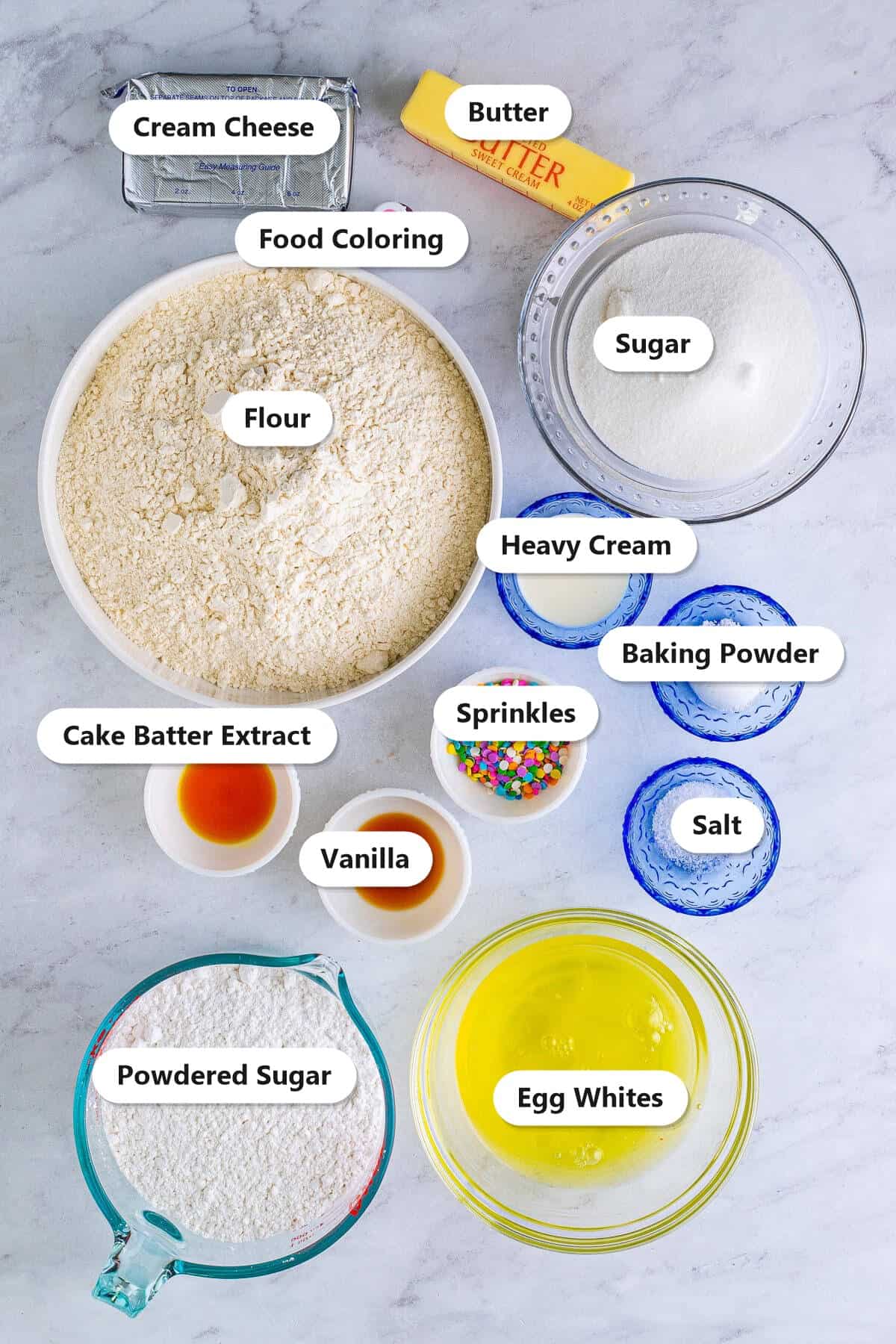 Labeled ingredients to make confetti cake cookies including flour, butter, sugar, egg whites, cake batter extract, sprinkles, cream cheese, and powdered sugar.