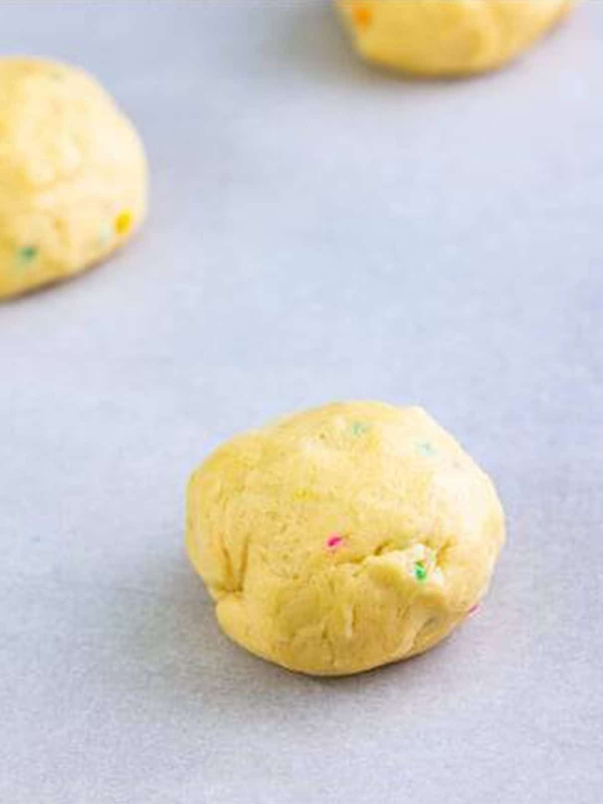 A smooth ball of confetti cake cookie dough rolled and placed on a parchment lined sheet.
