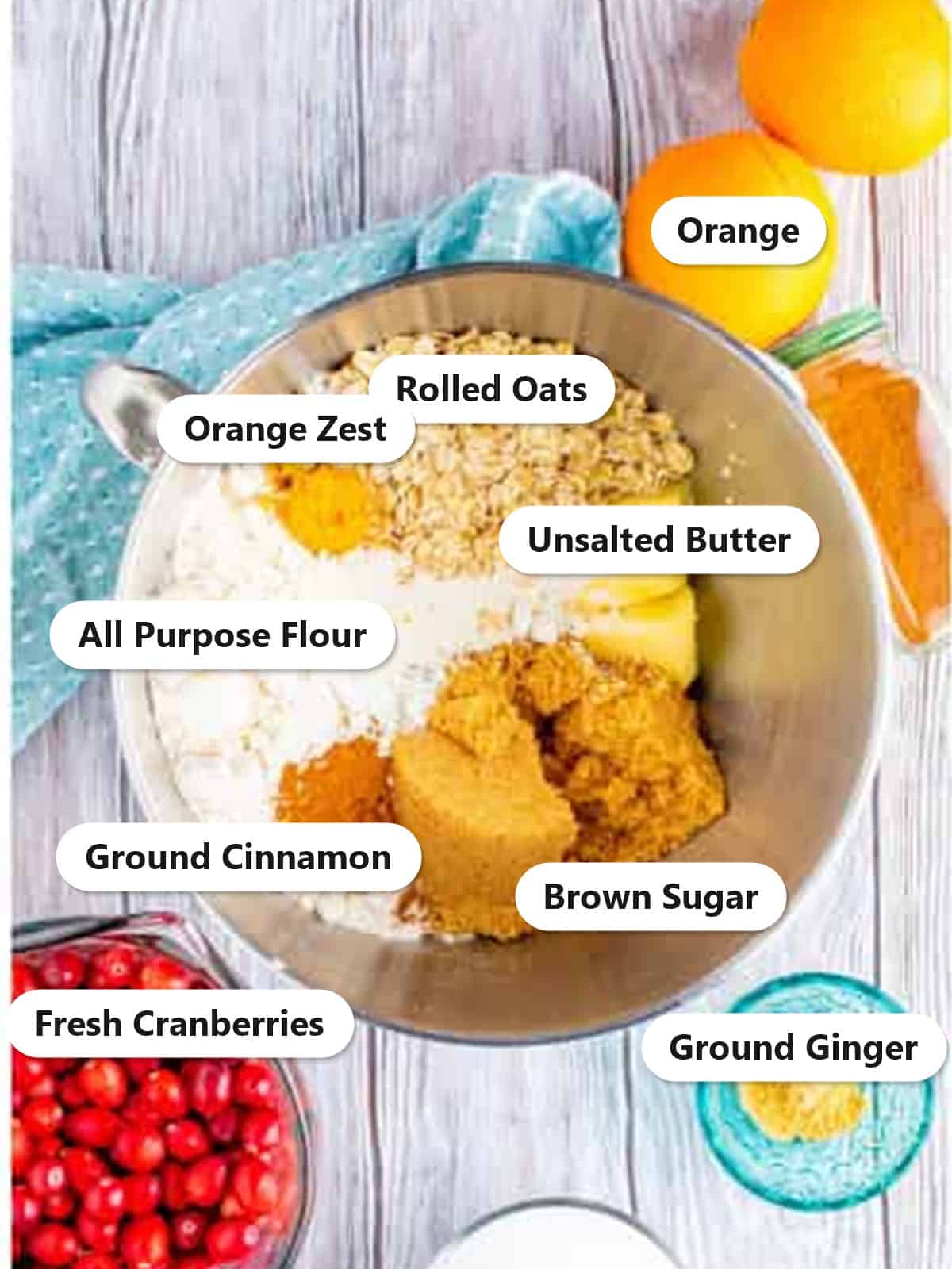 Labeled ingredients for cranberry bars including rolled oats, flour, brown sugar, butter, orange zest, cinnamon, fresh cranberries, orange, and ground ginger.