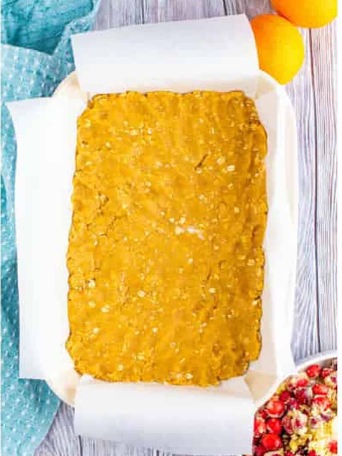 Oat crust pressed evenly into a parchment lined 9x13 baking dish for cranberry bars.