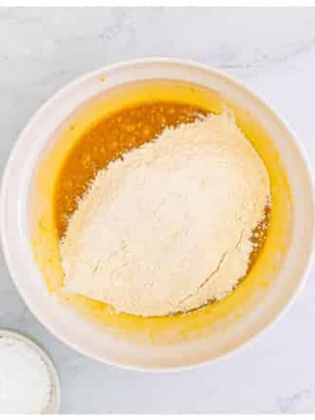 Flour and ginger being added to blondie batter for cranberry bliss bars.