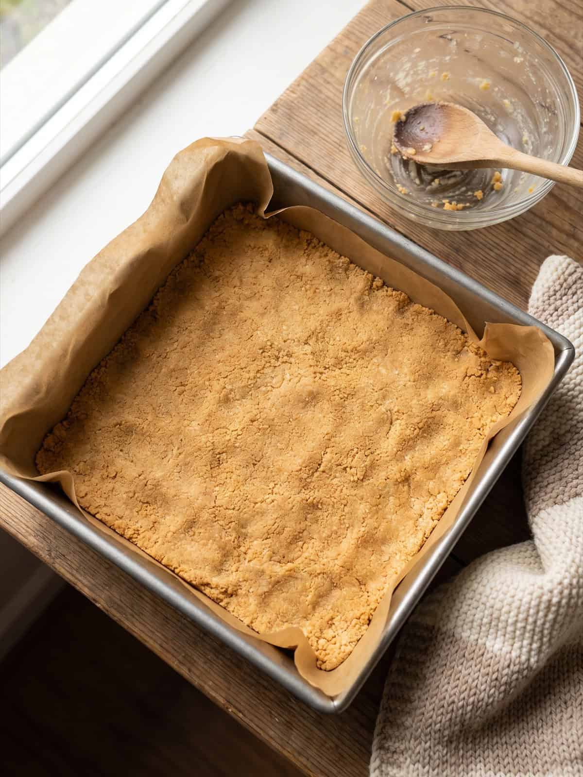 Golden cookie crust pressed into a square baking pan.