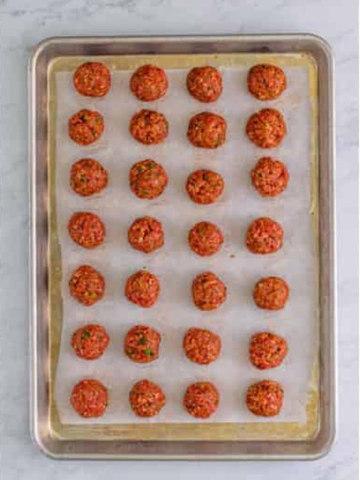Rolled Cranberry Meatballs lined up on a parchment lined sheet tray.