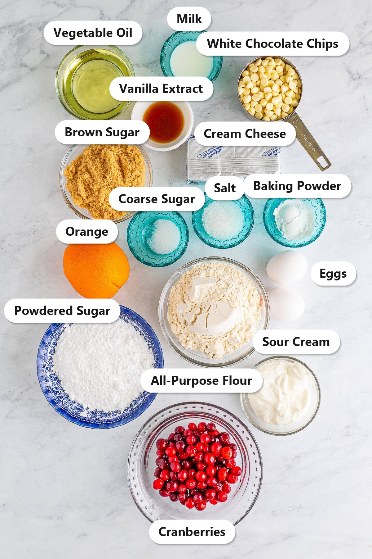 Labeled ingredients for Cranberry Orange Muffins including flour, cranberries, white chocolate chips, orange, sour cream, and cream cheese.