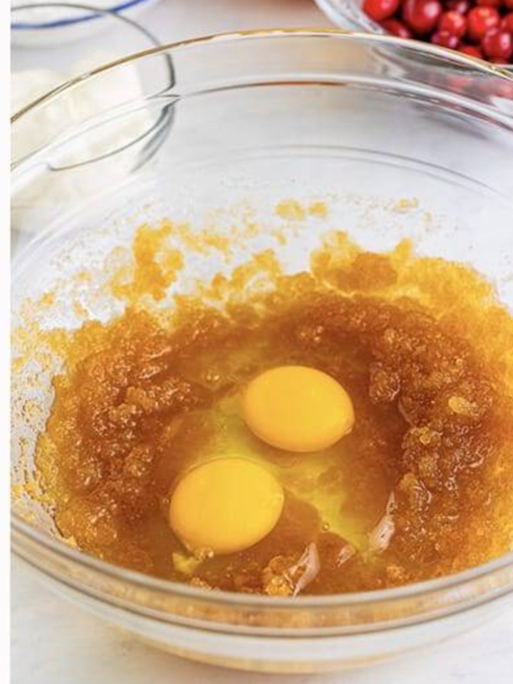 Eggs added to whisked oil and brown sugar for Cranberry Orange Muffins.