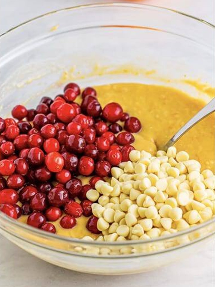 Folding fresh cranberries and white chocolate chips into Cranberry Orange Muffins batter.