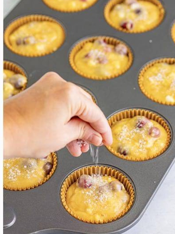 Sprinkling coarse sugar over Cranberry Orange Muffins batter in the muffin tin.
