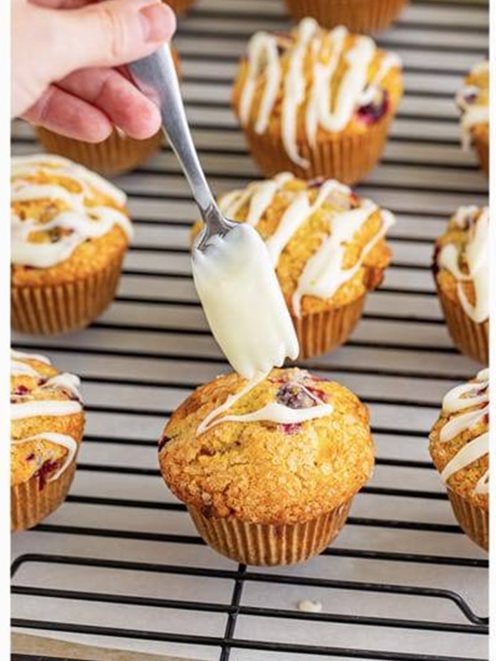 Drizzling white chocolate cream cheese glaze over baked Cranberry Orange Muffins.
