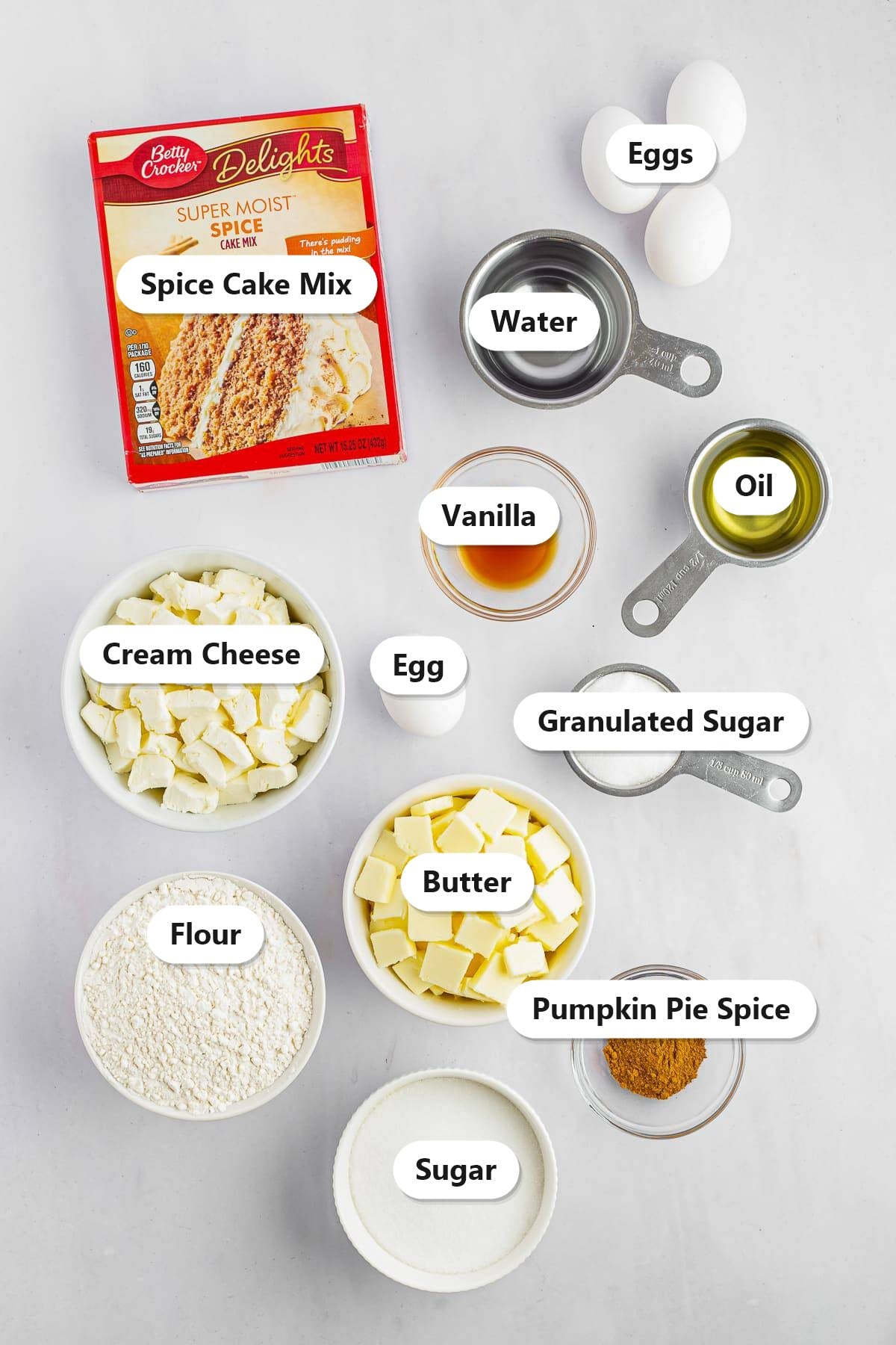 Labeled ingredients to make cream cheese crumb cake including spice cake mix, cream cheese, butter, flour, sugar, and pumpkin pie spice.