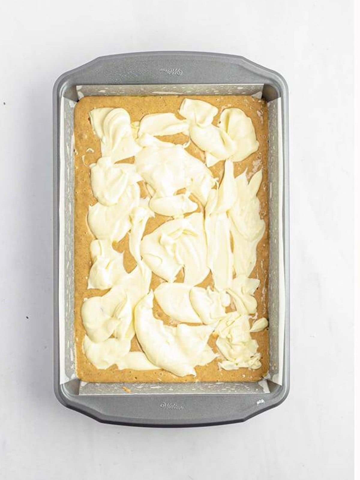 Cream cheese filling dolloped over the cake batter in the pan for cream cheese crumb cake.