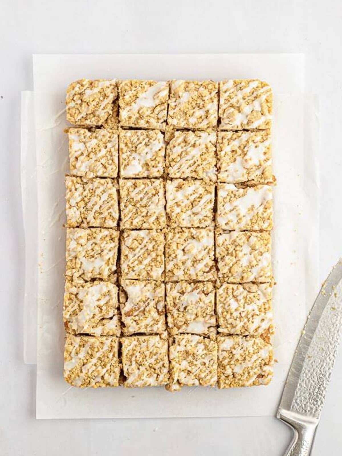 Glazed cream cheese crumb cake cut into squares on parchment paper.
