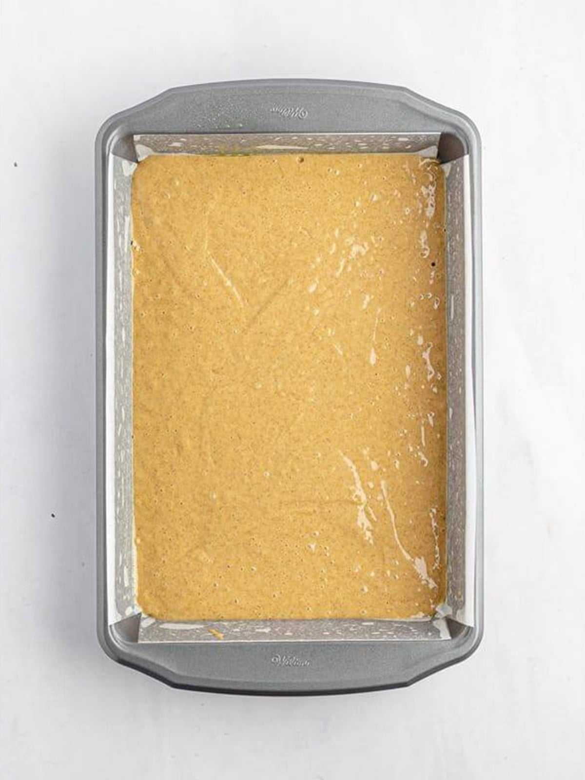 Spice cake batter spread evenly in a baking pan for cream cheese crumb cake.