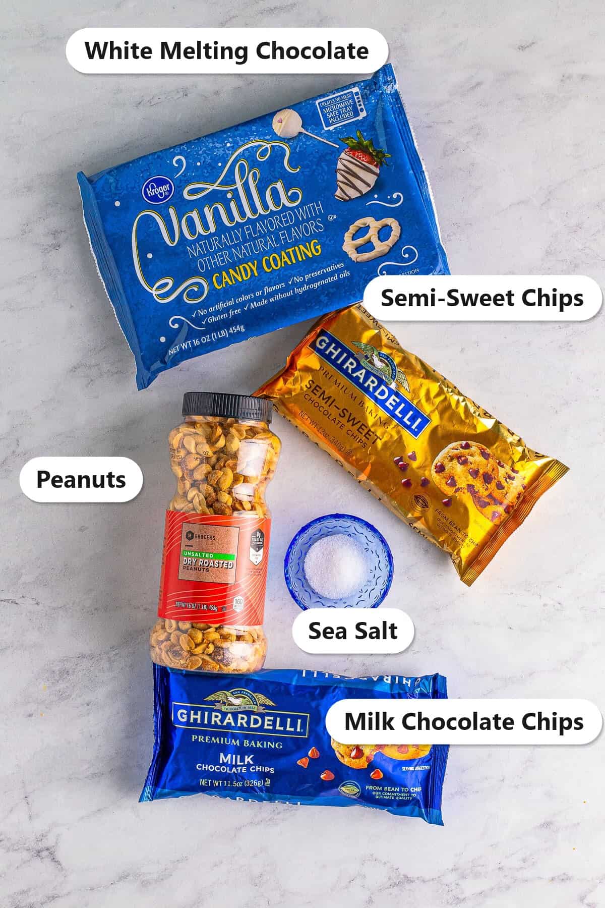 Labeled ingredients to make crockpot candy including white melting chocolate, semi-sweet chips, milk chocolate chips, dry roasted peanuts, and sea salt
