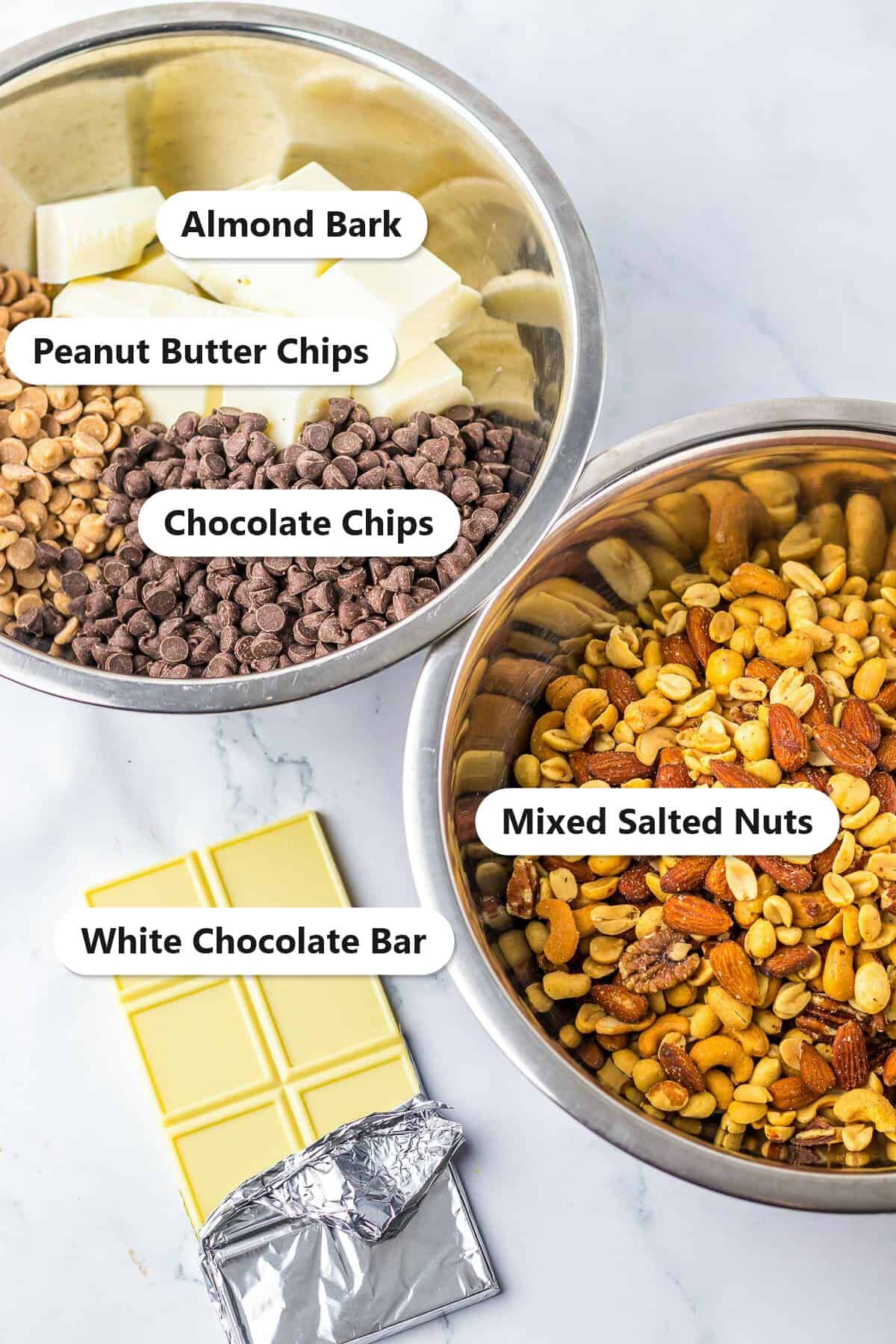 Labeled ingredients to make Crockpot Candy: almond bark, peanut butter chips, chocolate chips, mixed salted nuts, and a white chocolate bar.