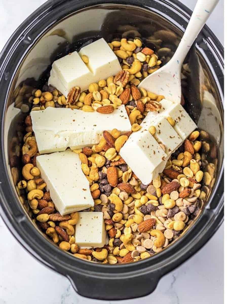 Almond bark, chocolate chips, peanut butter chips, and mixed nuts added to the slow cooker for Crockpot Candy.