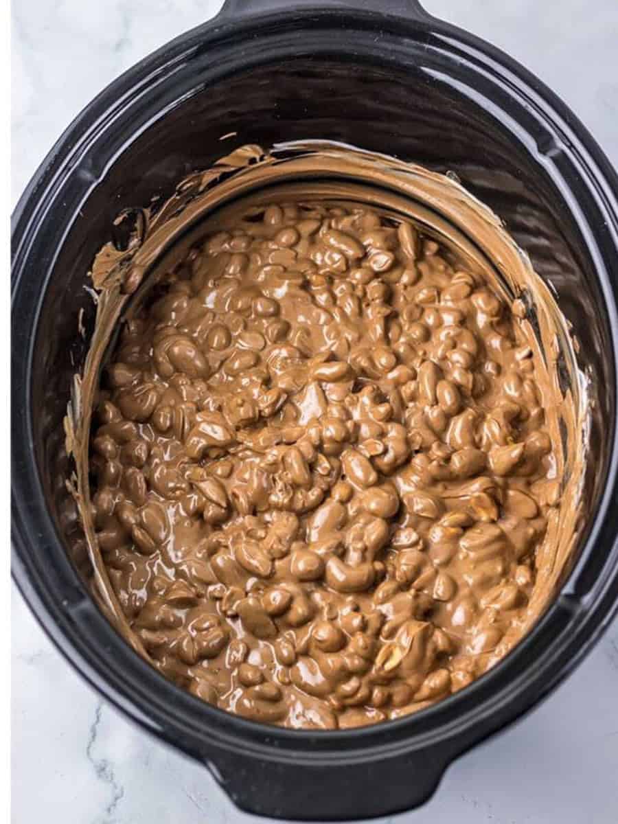 Melted chocolate and nut mixture stirred together in the slow cooker for Crockpot Candy.