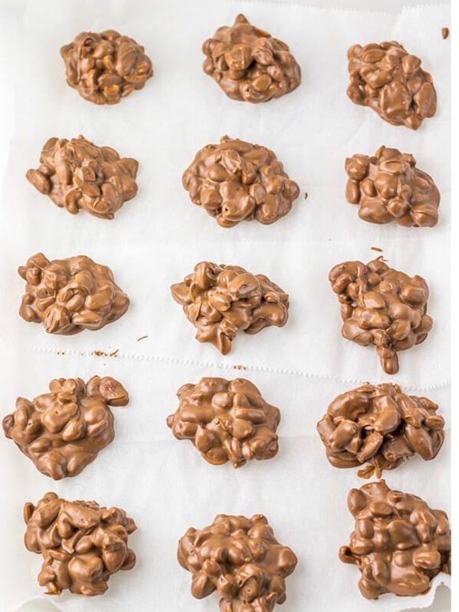 Spoonfuls of Crockpot Candy clusters set onto parchment paper to cool.