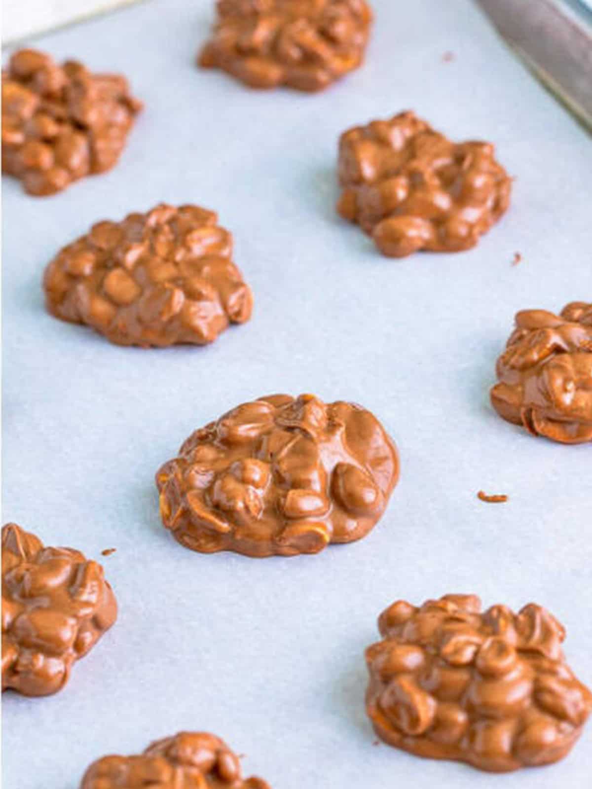 Tablespoon dollops of crockpot candy placed on parchment lined sheet trays