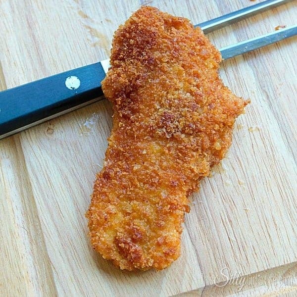Crispy crouton chicken strip on a wooden cutting board with a golden crunchy crust.