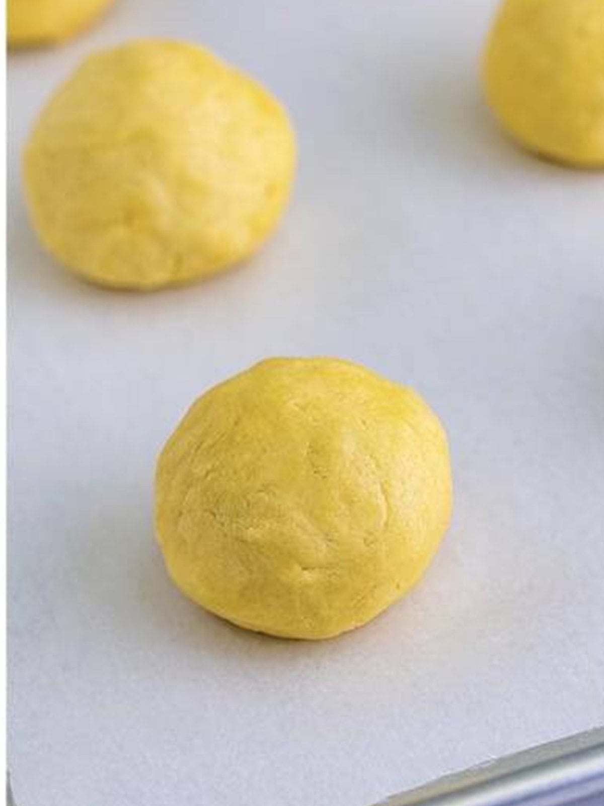 Cookie dough portioned and rolled into large smooth balls on a parchment lined tray.