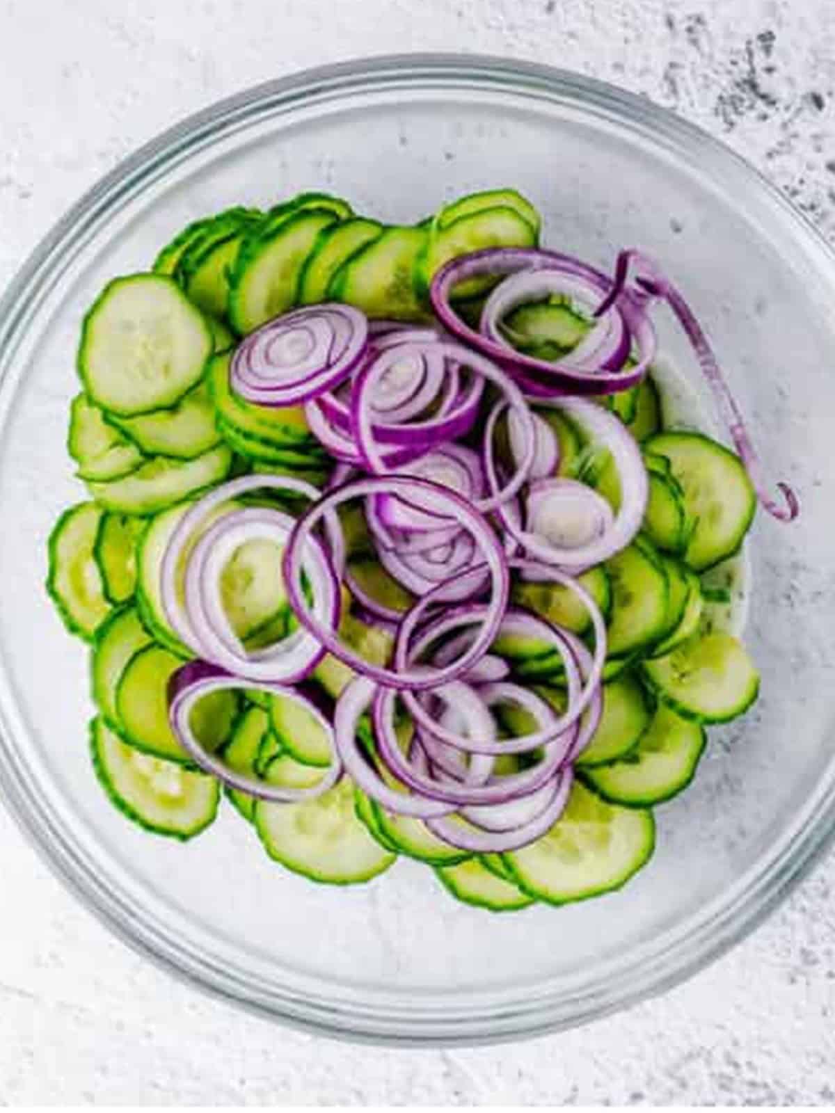 Dried cucumber slices and red onion added to the bowl of creamy dill dressing for Cucumber Dill Salad.
