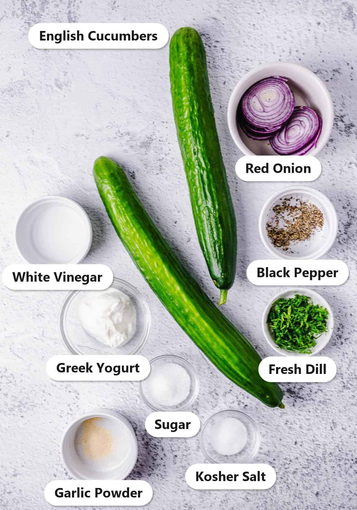 Labeled ingredients for Cucumber Dill Salad: English cucumbers, red onion, Greek yogurt, fresh dill, white vinegar, sugar, garlic powder, kosher salt, and black pepper.