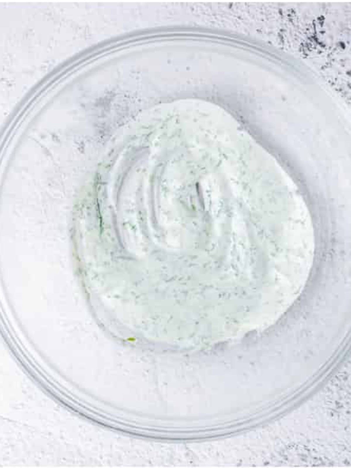 Greek yogurt dressing with fresh dill, vinegar, and seasonings stirred together in a bowl for Cucumber Dill Salad.