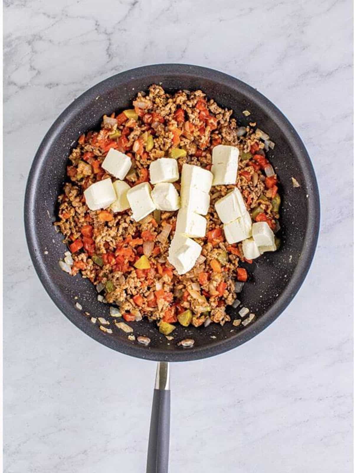 Cubed cream cheese added on top of the cooked beef and tomato mixture in a skillet.