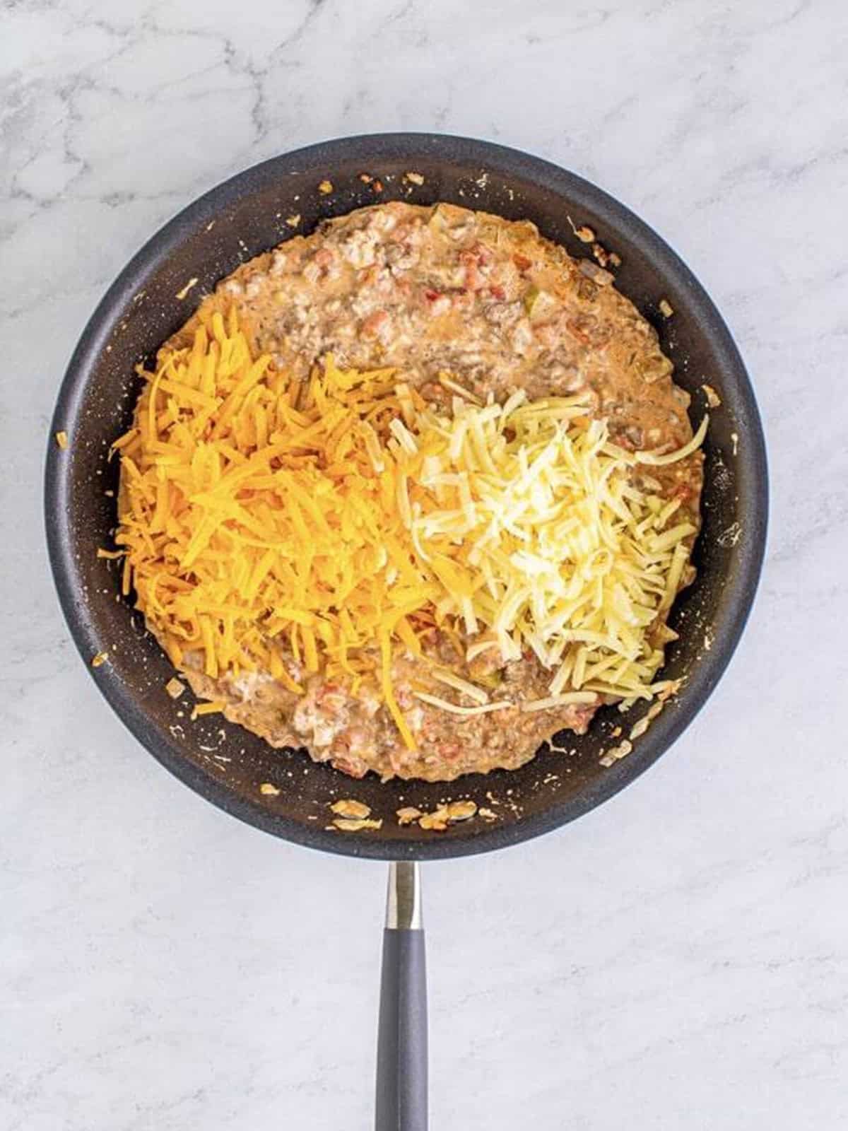 Shredded cheddar and Monterey Jack cheese added on top of the creamy dip mixture in a skillet.